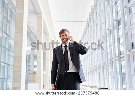 Corporate executive smiling at the camera while talking on his phone and walking down a corridor