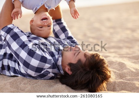 Little boy toddler laughing as his dad is playing by turning him upside down
