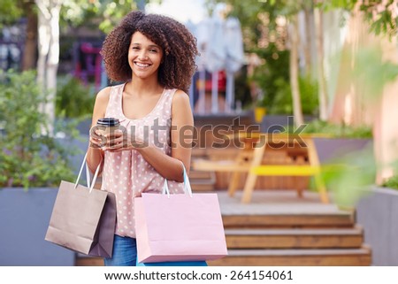 A young woman holding shopping bags and coffee outdoors
