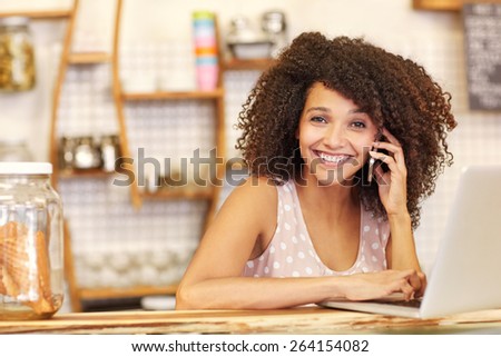 A young woman working on her laptop while speaking on the phone in a coffee shop