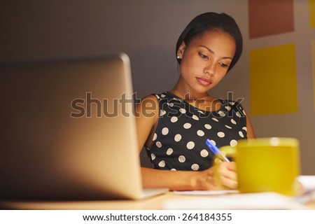 A young woman writing while sitting in her office at night
