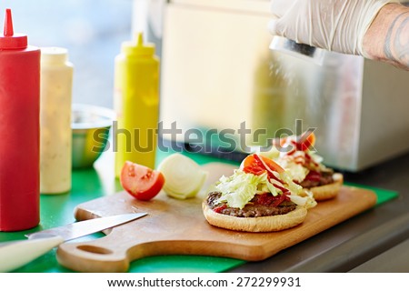 Open hamburger on a wooden board with tomato sauce and mustard dispensers alongside