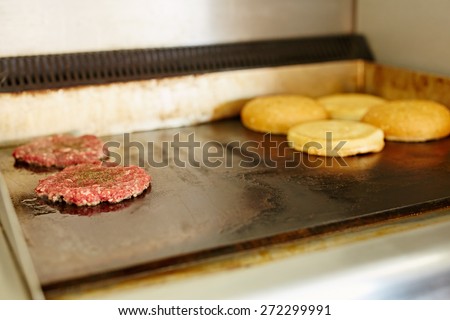 Two burger patties frying next to each other with open buns being toasted nearby