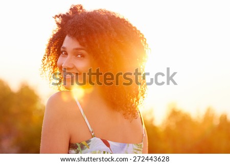 Beautiful mixed race woman looking back over her shoulder happily smiling at the camera with goldern sun flare