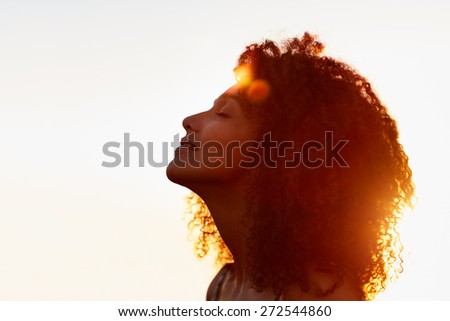 Profile protrait of a beautiful woman with afro style hair silhouetted against golden sun flare on a summer evening