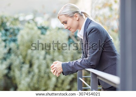 A young businesswoman leaning against the railing of her office balcony
