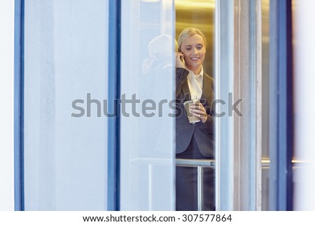 A young businesswoman talking on the phone in the elevator, seen through window
