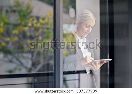 A young businesswoman seen working on tablet through her office window