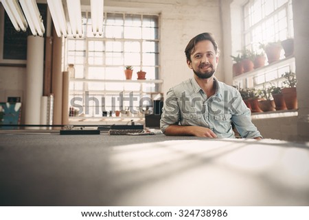 Portrait of a small business owner sitting casually in his worskhop studio looking confident and positive