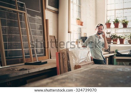 Small business owner talking on his phone while smiling and standing casually in his studio workshop