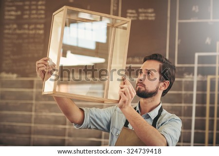 Designer looking carefully at a new product made from glass and wood in preparation for entrepreneurial marketing