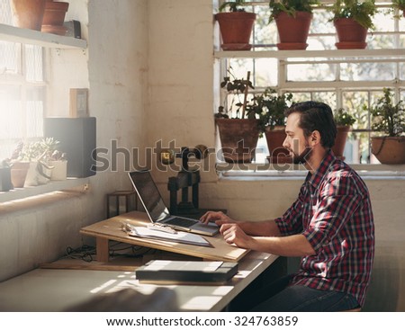 Young designer typing on his laptop while sitting in a creative space that he uses as his office in his studio