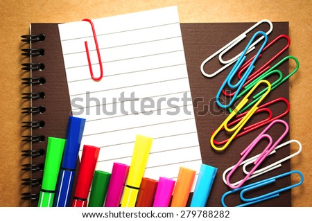 Note paper clip on notebook with colorful marker pens and paperclips on brown cardboard background
