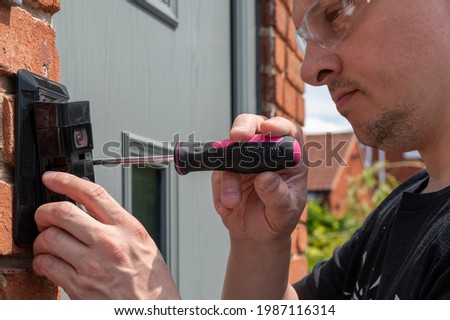 Man installing a smart doorbell with security camera and solar charger next to the front door of his house