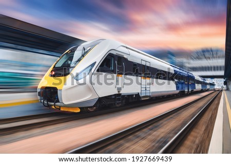 High speed train in motion on the railway station at sunset. Modern intercity passenger train with motion blur effect on the railway platform. Industrial. Railroad transportation in Europe