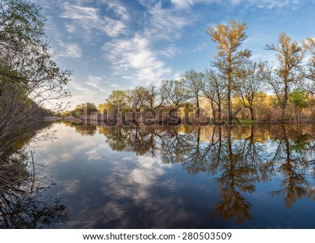 Beautiful sunset on the river in forest with sky reflection. Spring in Ukraine