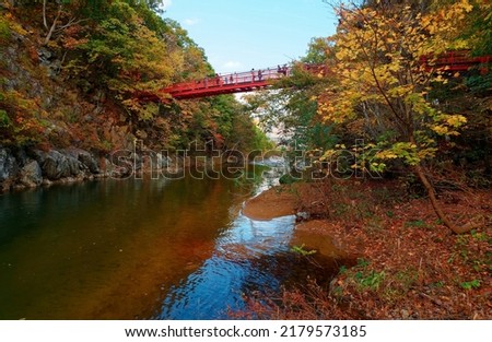 Scenery of the red Futami suspension bridge over Toyohira River with beautiful fall colors on the riverside cliffs in Jozankei (定山渓), a famous Onsen (hot spring) destination in Sapporo Hokkaido, Japan 商業照片 © 