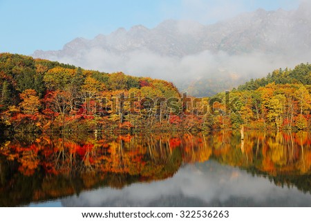 Autumn lake Scenery. Forests of colorful foliage reflected on Kagami Ike ( Mirror Pond ) with Mountain Togakusi in the foggy background in Nagano, Japan