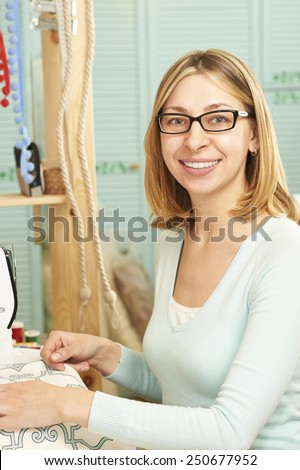 Young woman is sewing on sewing machine and smiling into camera