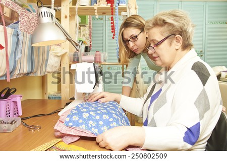 Experienced seamstress is teaching her assistant to work on sewing machine at workshop