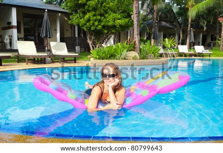 Sexy woman relaxing in outdoor swimming pool on air mattress. Front view