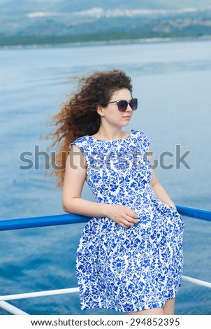 Beautiful young woman with long curly hairs on the ship. Beautiful smiling girl on the ship. Curly girl in summer.A beautiful young woman on a yacht at sea