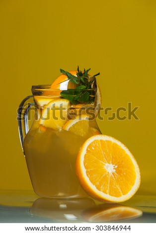 A fresh cool ice orange tea drink over yellow background.Fresh orange juice. Orange juice in pitcher and oranges