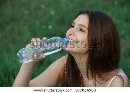 young beautiful brunette woman drinking a water from bottle in a park.Young woman drinking water at workout, outdoors