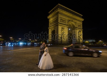 PARIS - SEPT 16, 2014: Wedding couple near the Arch of Triumph of the Star (The Arc de Triomphe de l'Etoile) and traffic lights at night. Paris, France.