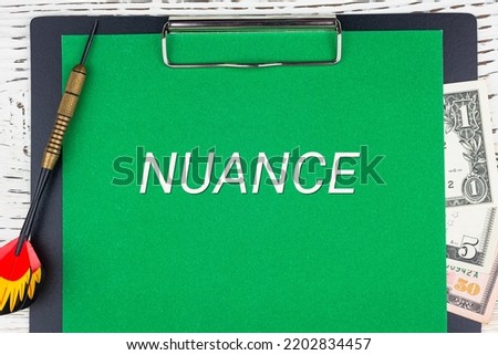 NUANCE - word (text), a dart for darts and dollar bills on a green background of a notebook, a wooden white table. Business concept: buying, selling, commerce (copy space). Photo stock © 