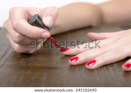 A hand applying red nail polish on the nails