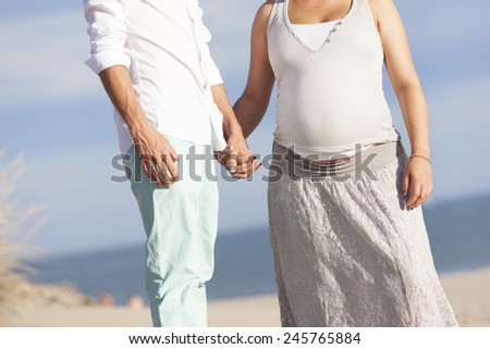 A pregnant woman and her husband holding their hands at the beach