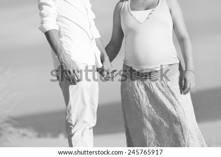 Black and white photo of a pregnant woman and her husband holding their hands at the beach