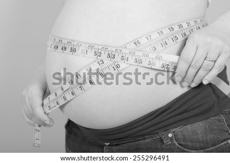 Black and white photo of a pregnant woman measuring her belly while standing