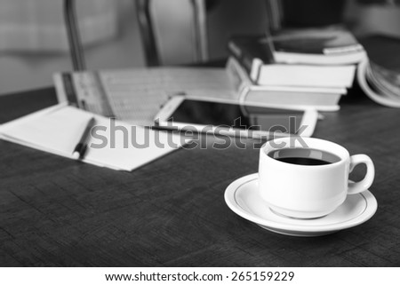 Black and white photo of a no name coffee cup and a stack of books in background on a wood table with shallow depth of field