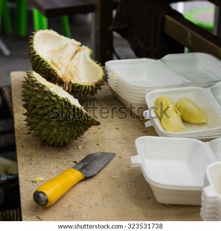 Peeled durian in pre-pack boxes, next to it is a knife, the tool to peel durian. Selective focus on the boxes, they are ready to sell as to-go, convenience fresh durian packs
