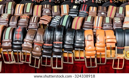 Set of different colors leather belts for men on display on red backdrop at street market in Bugis Village. This market is a good place to buy budget souvenirs in Singapore. Panoramic stye