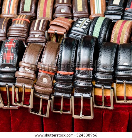 Set of different colors leather belts for men on display on red backdrop at street market in Bugis Village. This market is a good place to buy budget souvenirs in Singapore