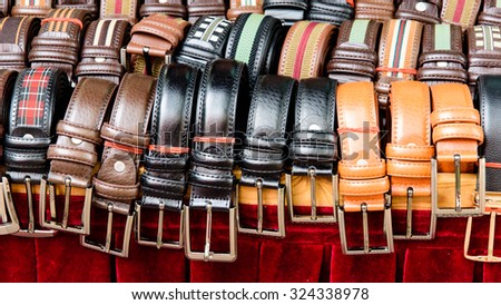 Set of different colors leather belts for men on display on red backdrop at street market in Bugis Village. This market is a good place to buy budget souvenirs in Singapore. Panoramic style
