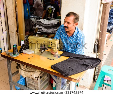 SINGAPORE OCT 26, 2015: An Indian man is repairing a sewing black fabric on an old sewing machine at the roadside of Little India in Singapore
