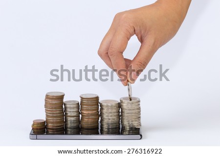 hand putting silver coins to piles of coins arranged as a graph on the smart phone.