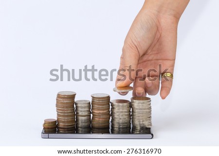 hand putting silver coins to piles of coins arranged as a graph on the smart phone.