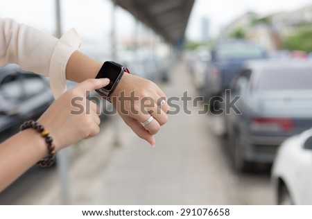 A female(woman) hand hold(touch) a smart watch on her left hand, background car park.
