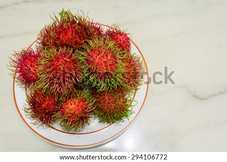 Red rambutan on white dish. Fruit tropical tree of the family Sapindaceae , native to South - East Asia , cultivated in many countries in the region, on marble background