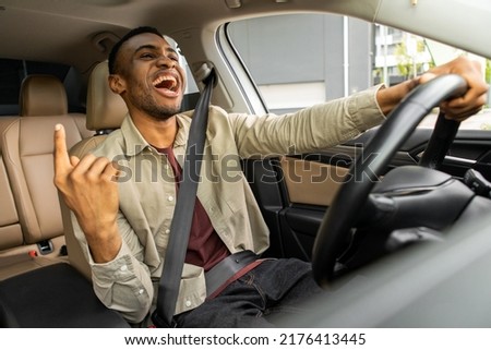 Joyful black man dancing in car, singing while driving his car. Road fun Foto stock © 