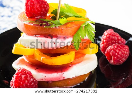 Closeup of tomato stack salad with fresh mozzarella, pepper and raspberry dressing on a black plate.
