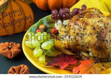 Close up of grilled whole chicken on thanksgiving dish with grapes and decoration stuff.