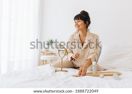 Woman doing skin care massage sitting on bed, Smiling woman using a roller to massage face.