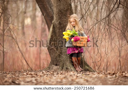 little girl with yellow flowers in the basket standing near the tree in the forest at spring time