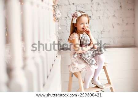 little smiling cute girl in beautiful dress is sitting with teddy bear in her hands